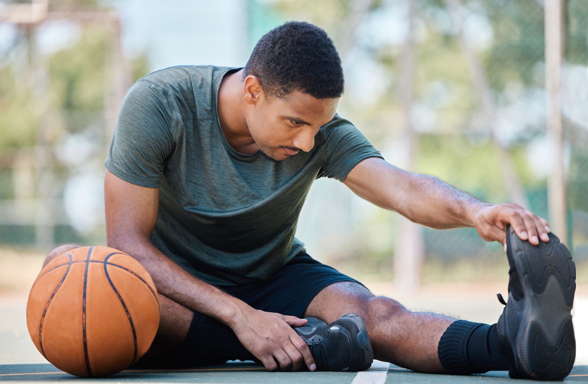 a man is sitting on the ground with a basketball and stretching his legs to prevent an ACL injury