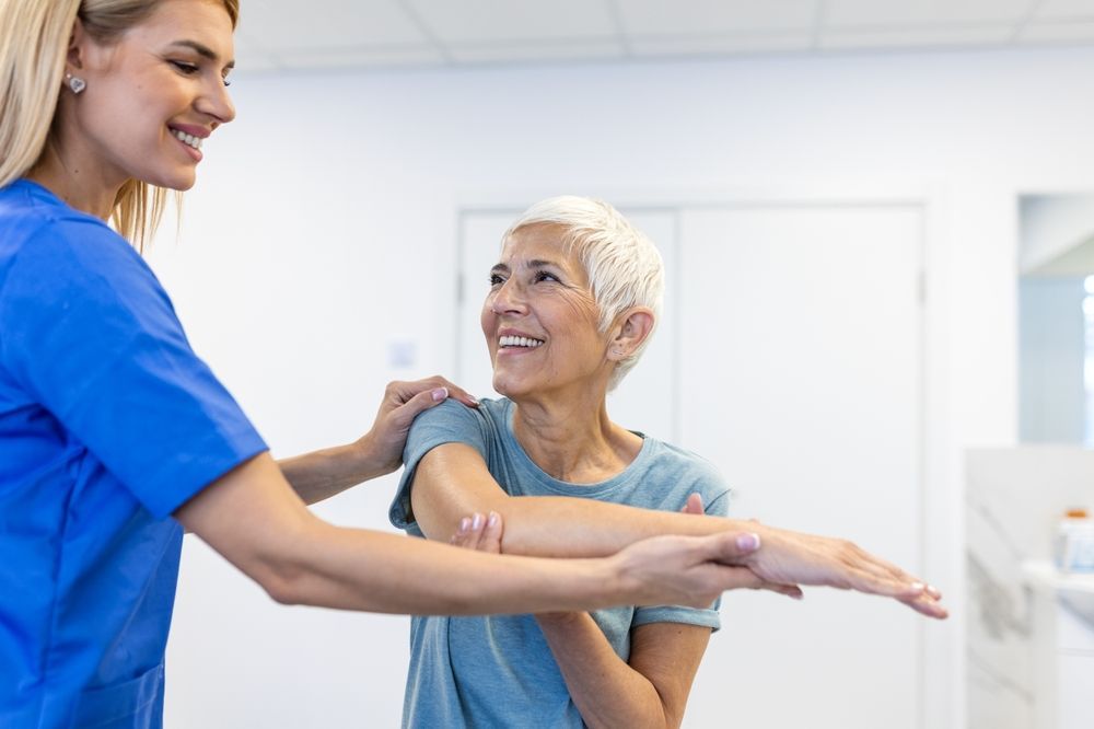 A physical therapist is helping an elderly woman stretch her arms.