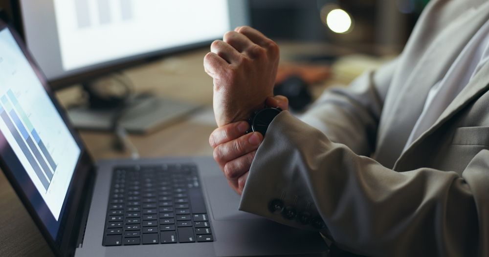 A man is holding his wrist in pain while using a laptop computer.