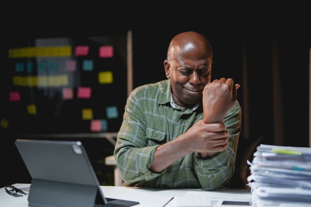 A man is sitting at a desk holding his wrist in pain with carpal tunnel