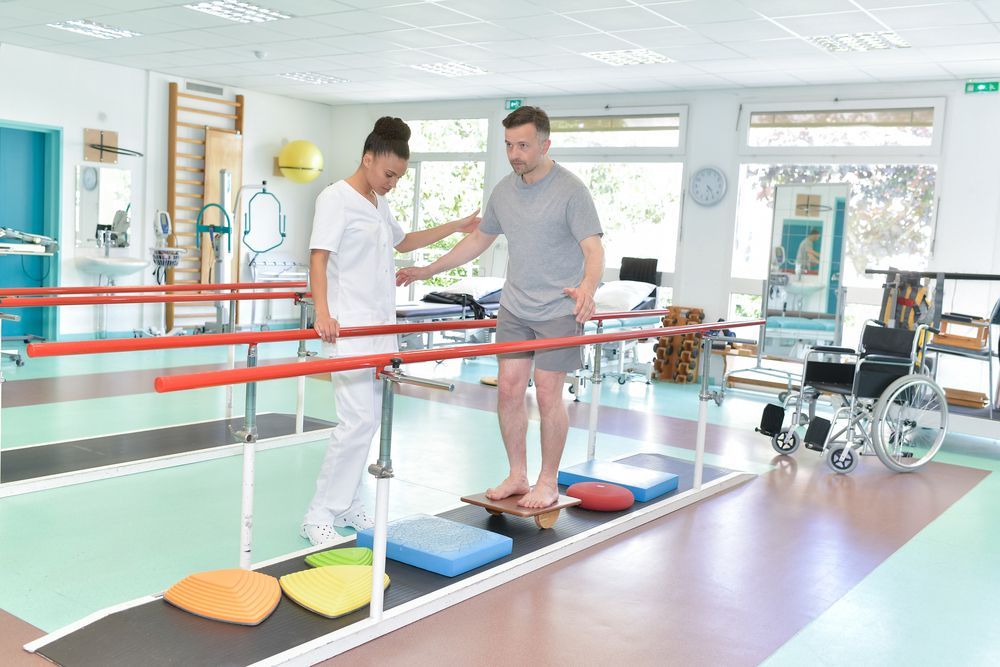 A nurse is helping a man walk on parallel bars in a gym.