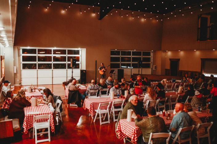 Dimly lit restaurant with people dining at red-and-white checkered tables under string lights.