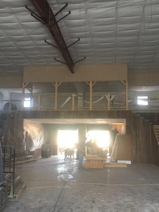 Interior of a large warehouse with high ceiling, overhead beam, bright open doorway, and construction materials scattered 