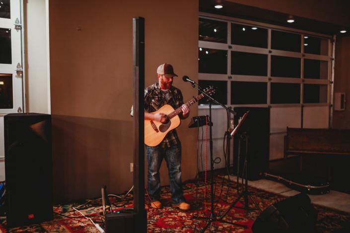 Musician singing and playing acoustic guitar on a small stage in a cozy indoor venue
