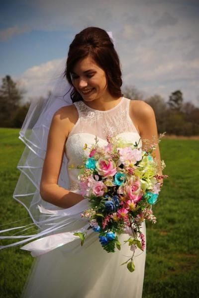Bride in a white wedding dress holding a colorful bouquet outdoors, smiling in the wind.