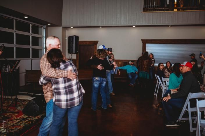 People dancing in a dimly lit hall while others watch from chairs along the wall.