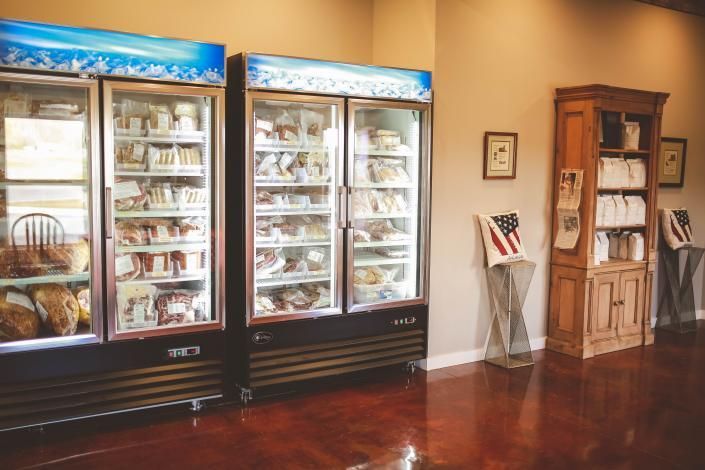 Refrigerated display cases in a shop, beside a wooden brochure cabinet and a wall with a small American flag display