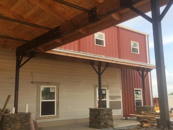Covered patio beside red and beige barn-style building with stone posts and wooden beams