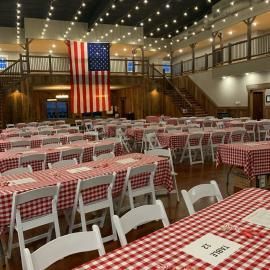 Decorated hall with rows of white chairs and checkered tables, and a large American flag hanging at the front