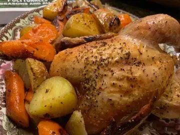 Roasted chicken with carrots and potatoes on a plate, seasoned with black pepper