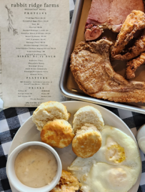 Breakfast plate with biscuits, eggs, gravy, fried meat, and a restaurant menu on checkered cloth