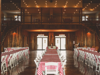 Indoor banquet hall with long red-checkered tables and white chairs under warm string lights