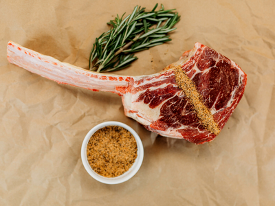 Raw ribeye steak with rosemary and a bowl of seasoning on brown paper