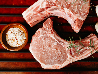 Raw pork chops with rosemary and coarse salt on a dark wooden board