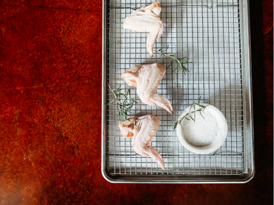 Three raw fish fillets and a white bowl of sauce on a wire rack over a red background