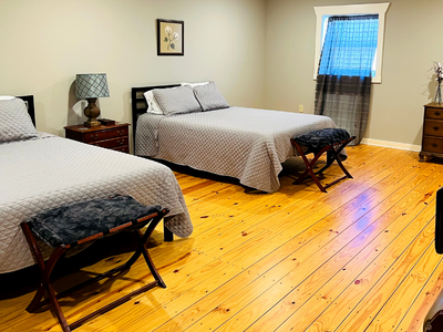 Bedroom with two beds, wooden floor, nightstands, and a blue window shade