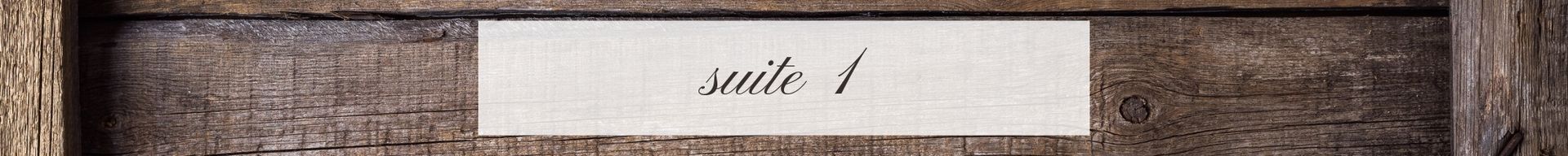 Close-up of a rustic wooden sign with a small white label reading “suite 1”