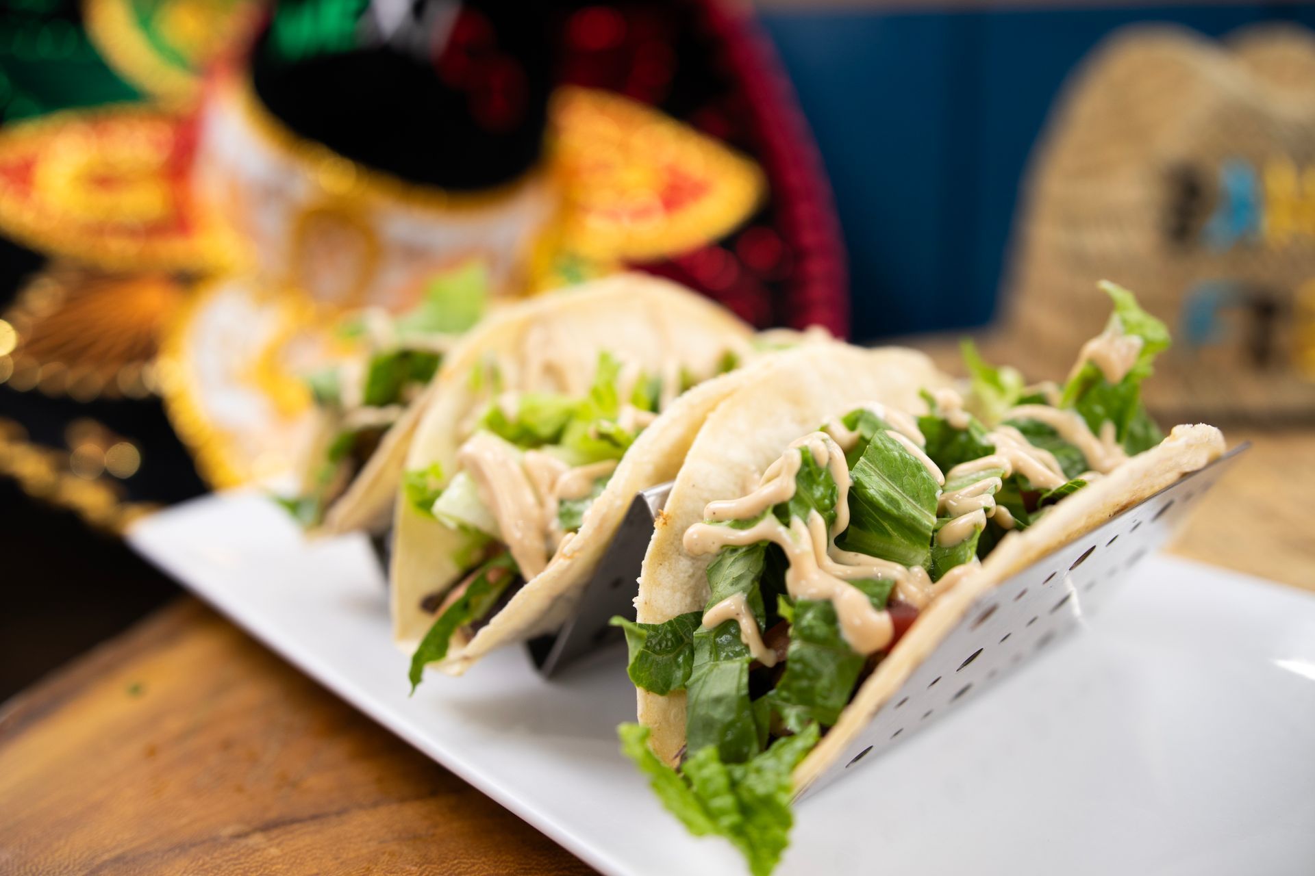 Three tacos are sitting on a white plate on a wooden table.