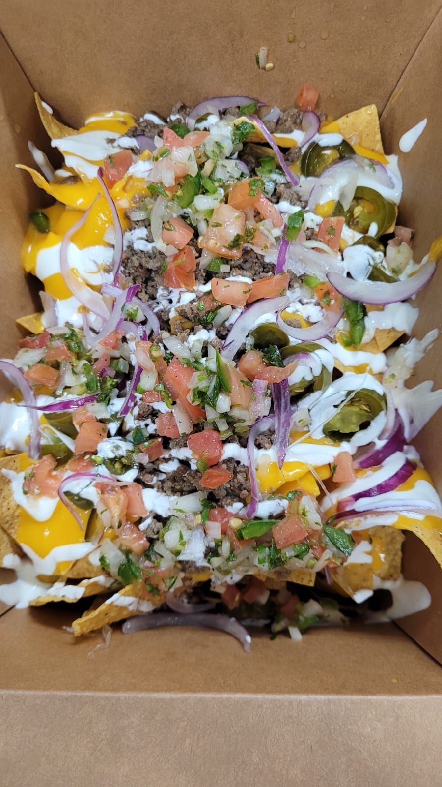 A box of nachos with a lot of toppings on them.