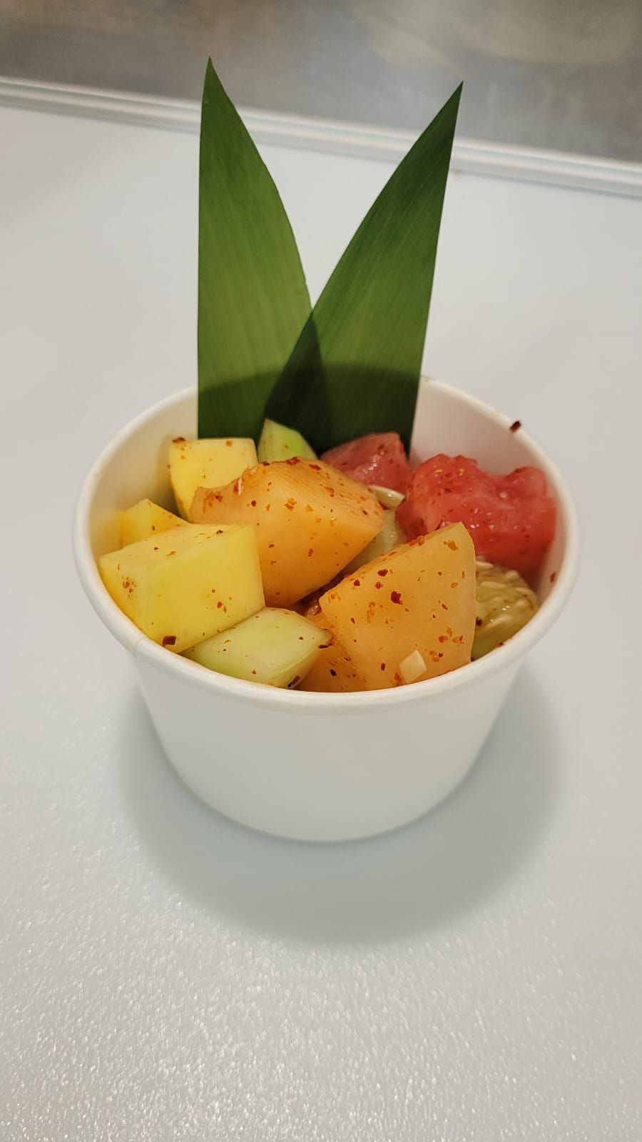 A bowl of fruit salad with a palm leaf on top.