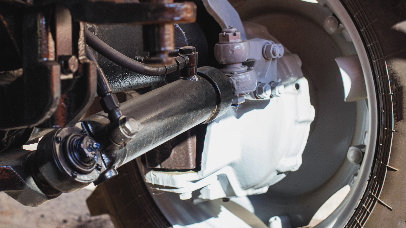 Close-up of a tractor wheel and steering components, painted light grey, with visible nuts and bolts.