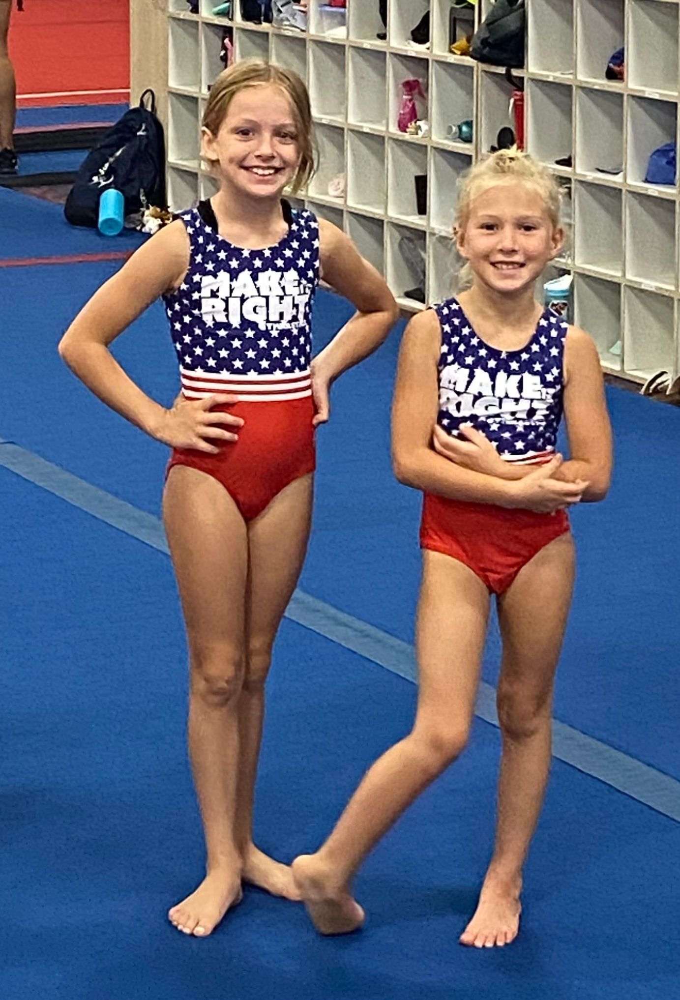Two gymnasts stand in red white and blue leotards in the gym