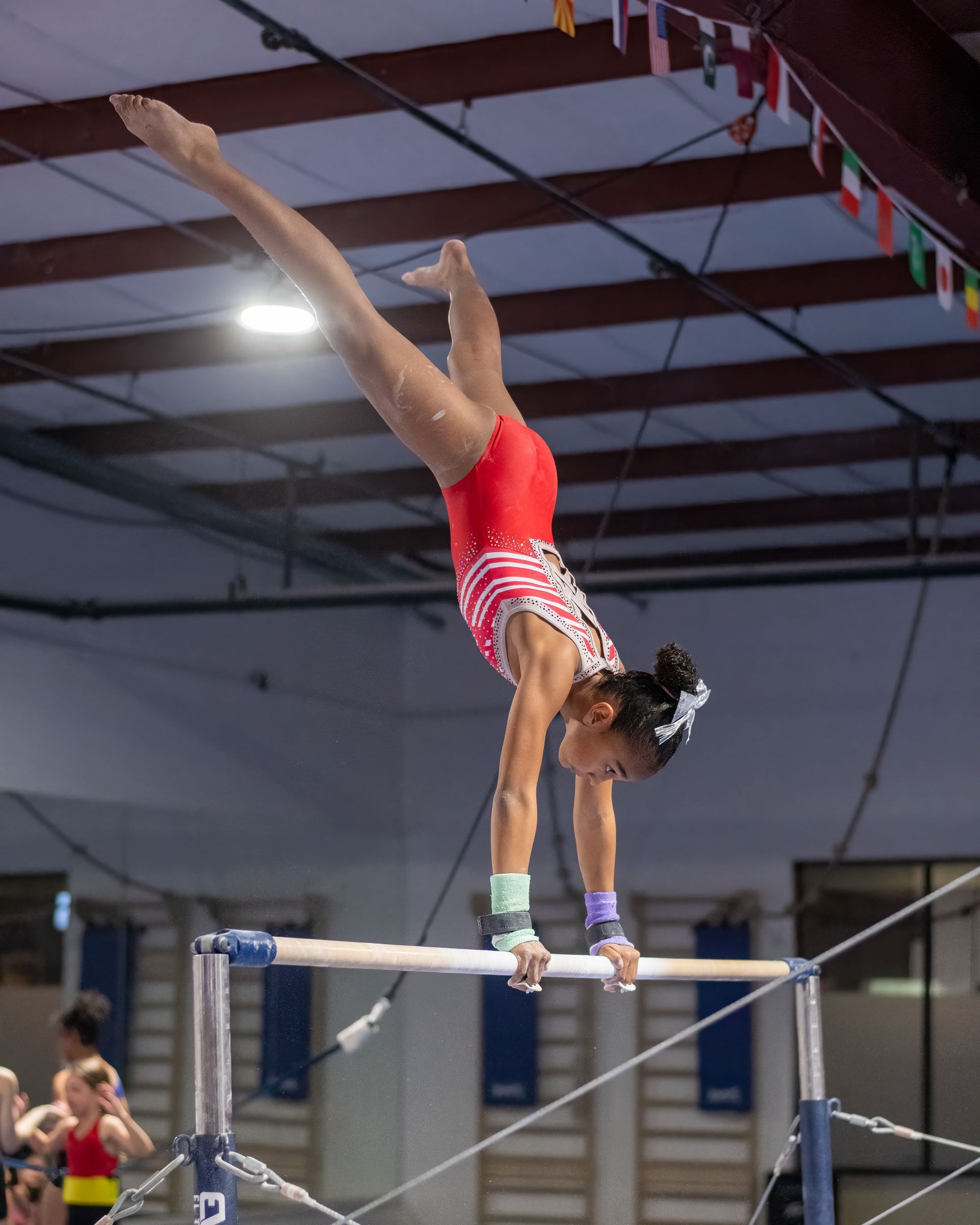 Gymnast on uneven bars, upside down in handstand, red and white leotard, gymnasium.