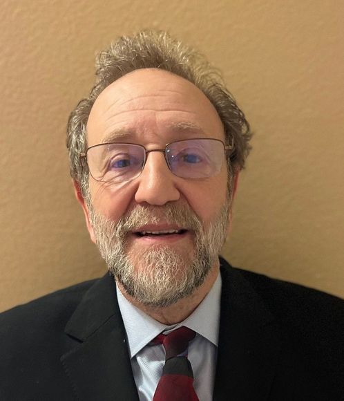 A man with a beard and glasses is wearing a suit and tie.