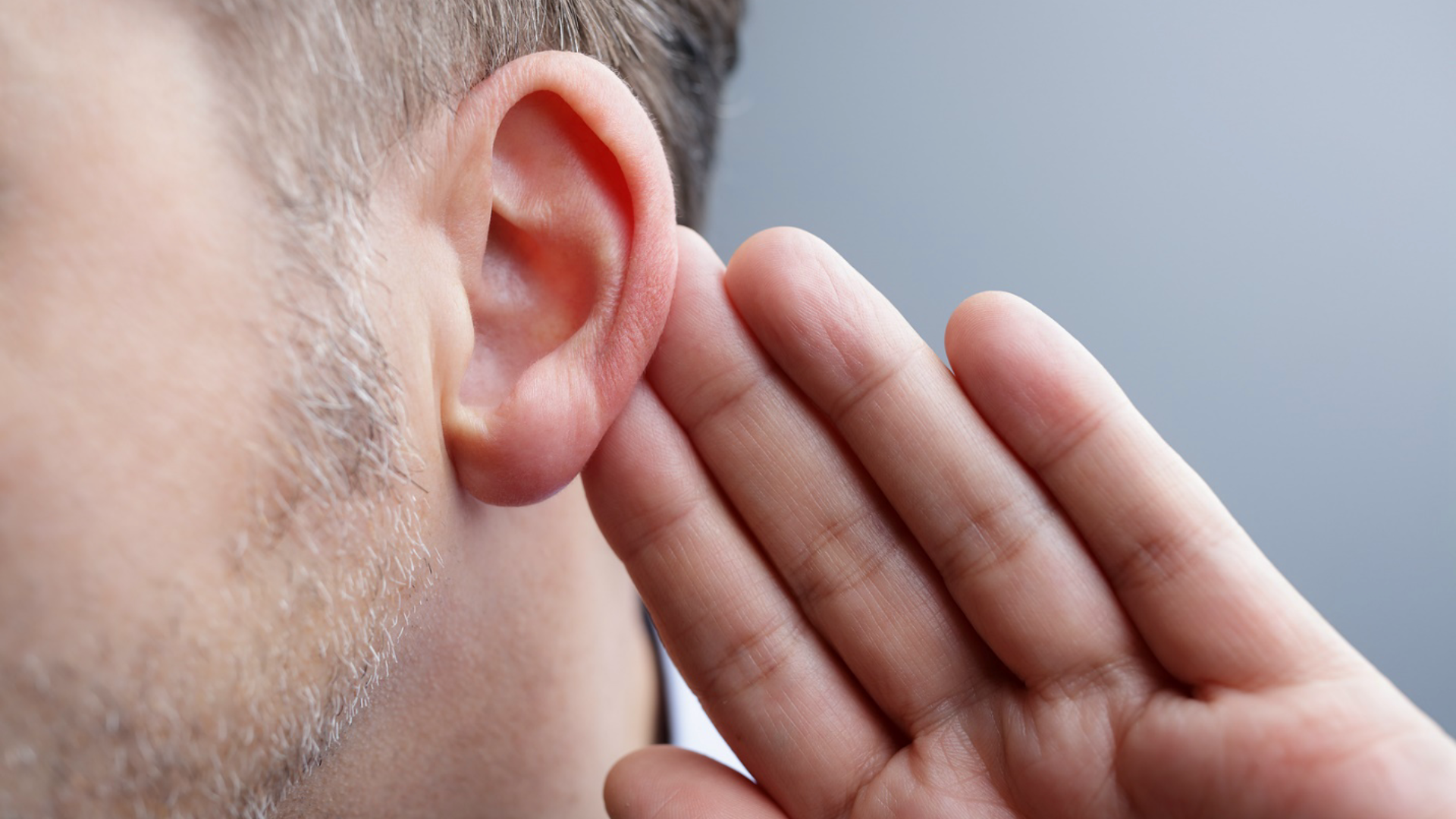 A man is holding his hand to his ear to hear something.