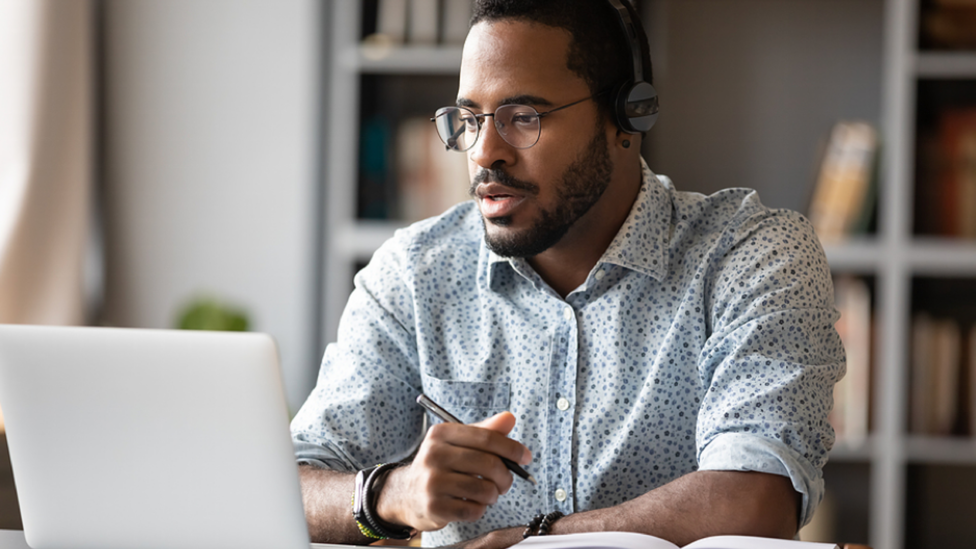 A man wearing headphones is sitting at a desk using a laptop computer.