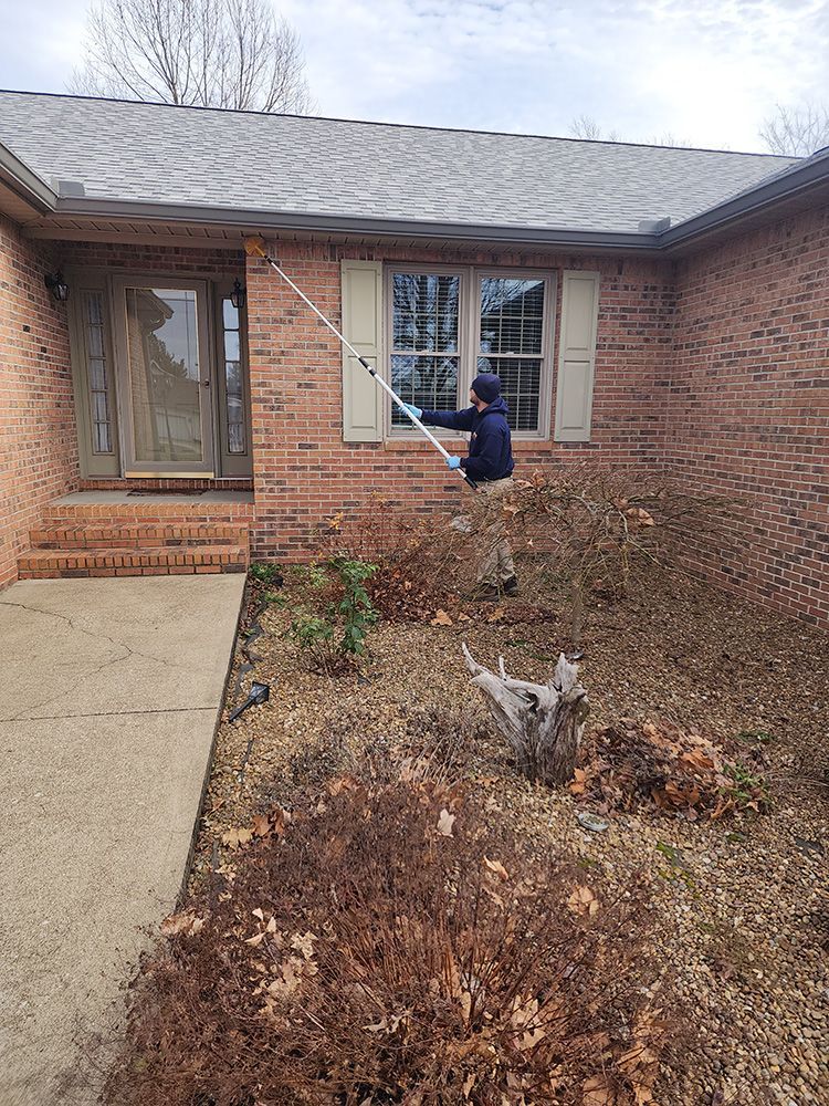 A man is cleaning the windows of a brick house.