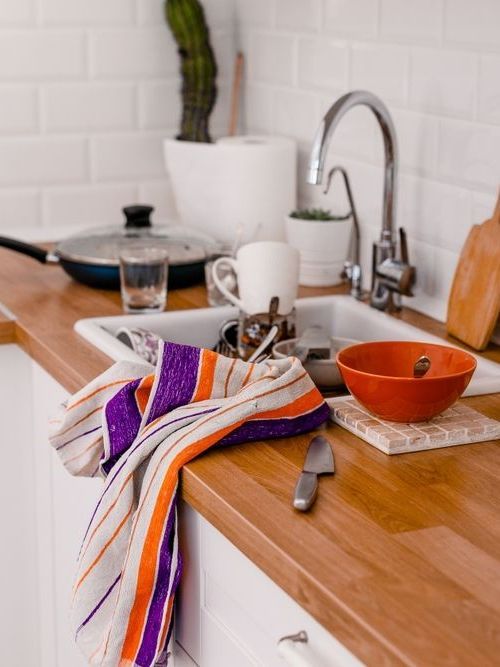 A kitchen counter with a sink , bowls , utensils and a towel on it.