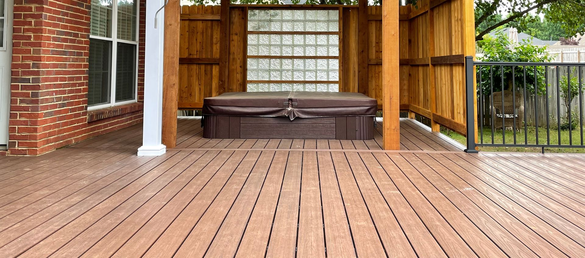 Brown composite deck with hot tub covered by gazebo, adjacent to a brick wall and railing.