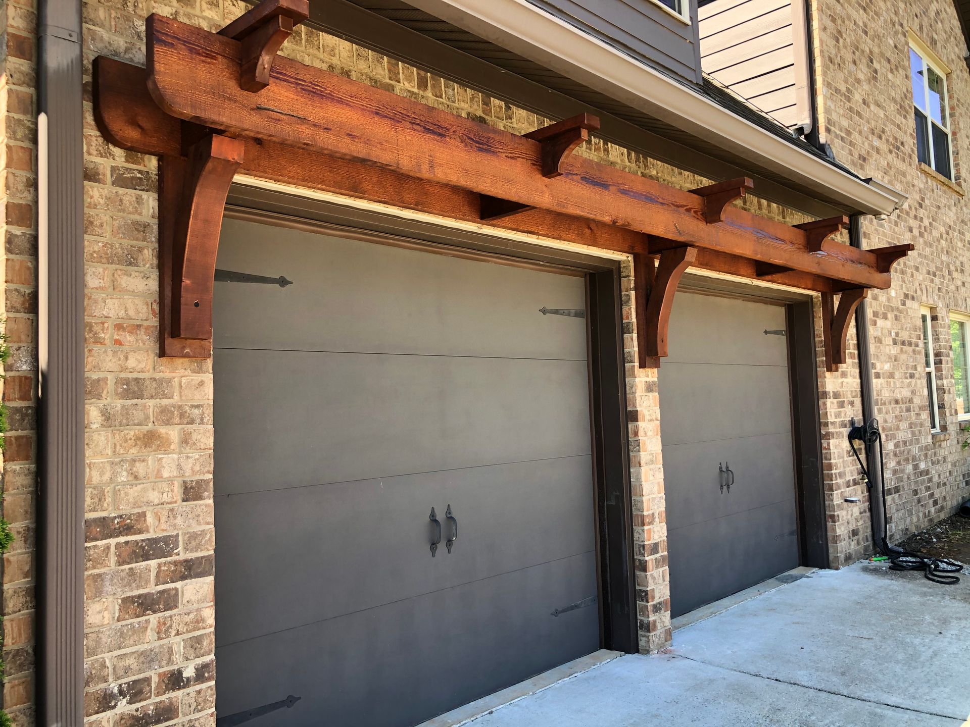 A brick building with two garage doors and a wooden pergola over them.
