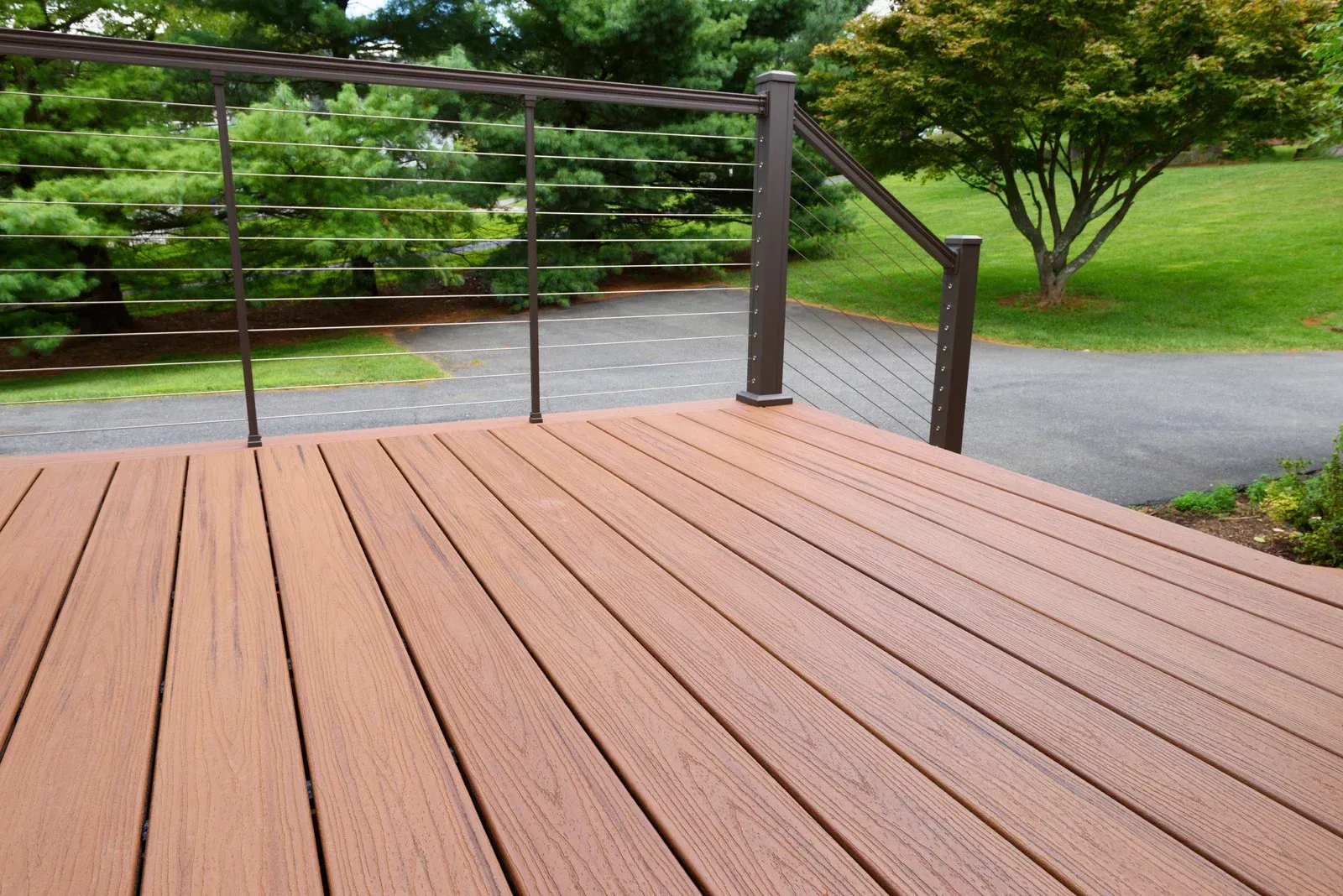 A wooden deck with a metal railing and trees in the background