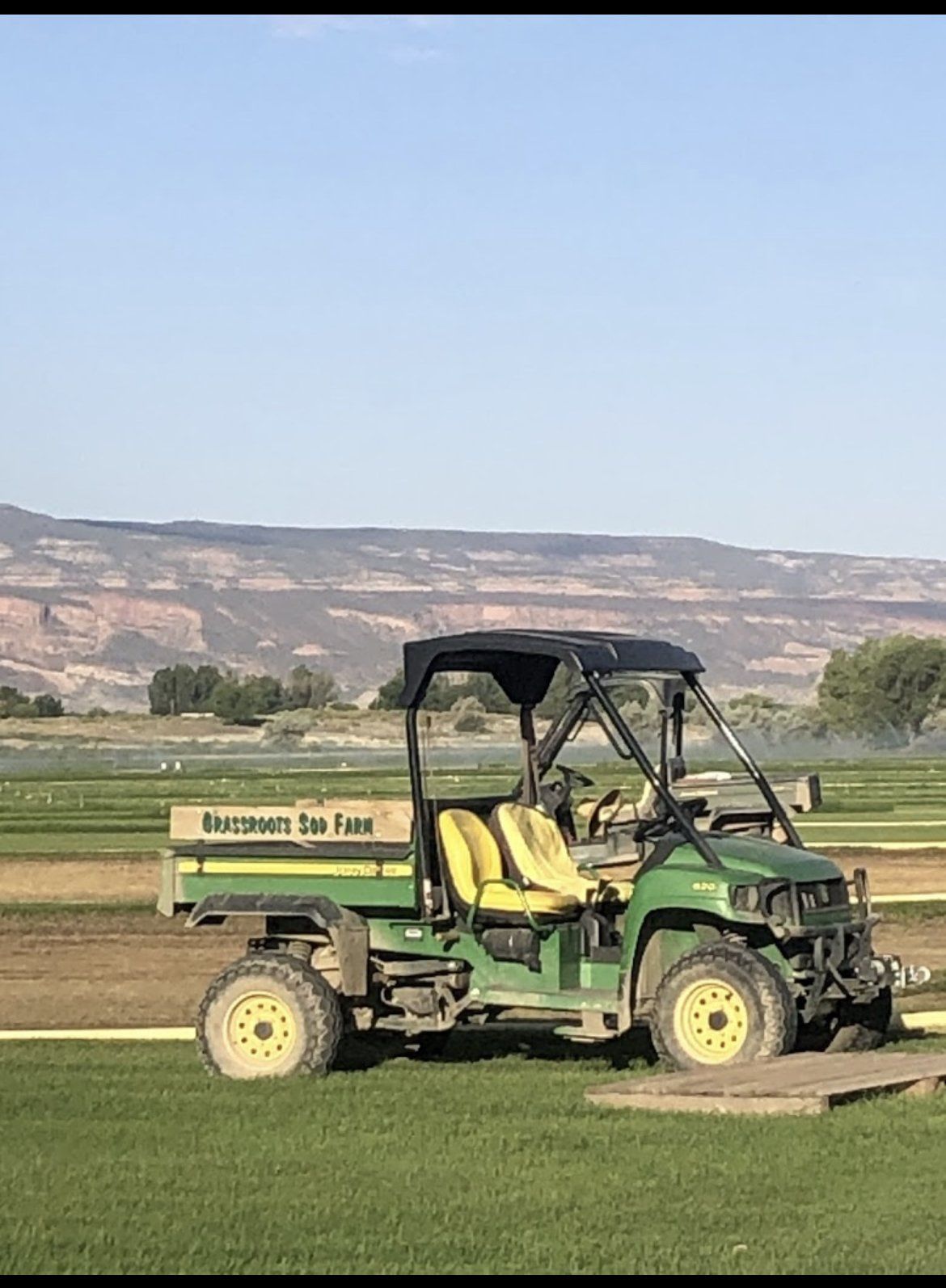 A green and yellow utility vehicle is parked on a lush green field.