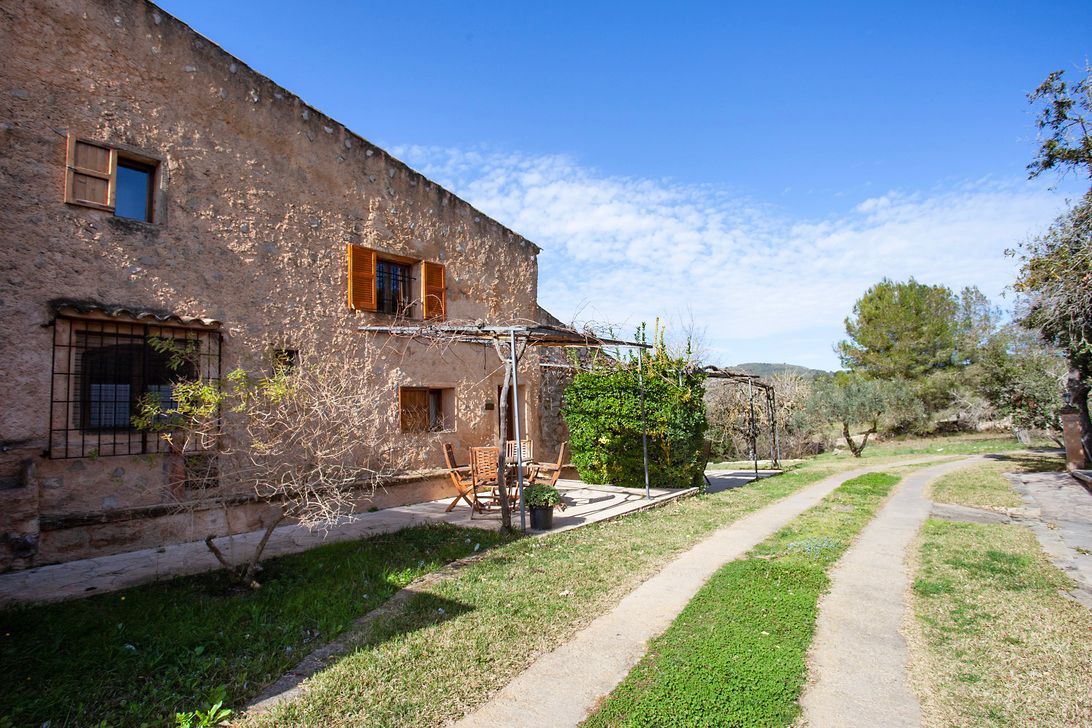 Una casa de piedra con un camino que conduce a ella está rodeada de césped y árboles.
