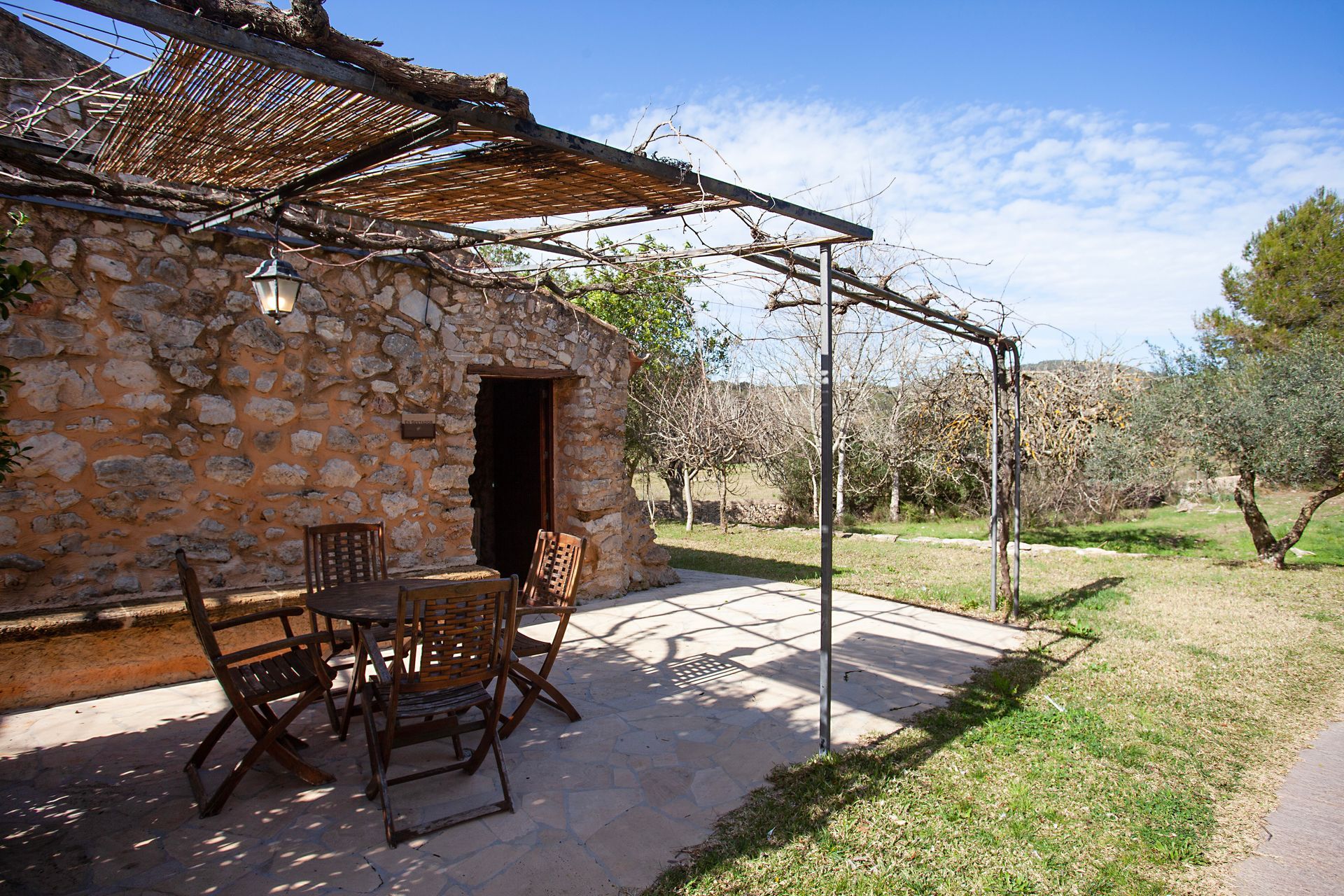 Un edificio de piedra con una mesa y sillas bajo una pérgola.