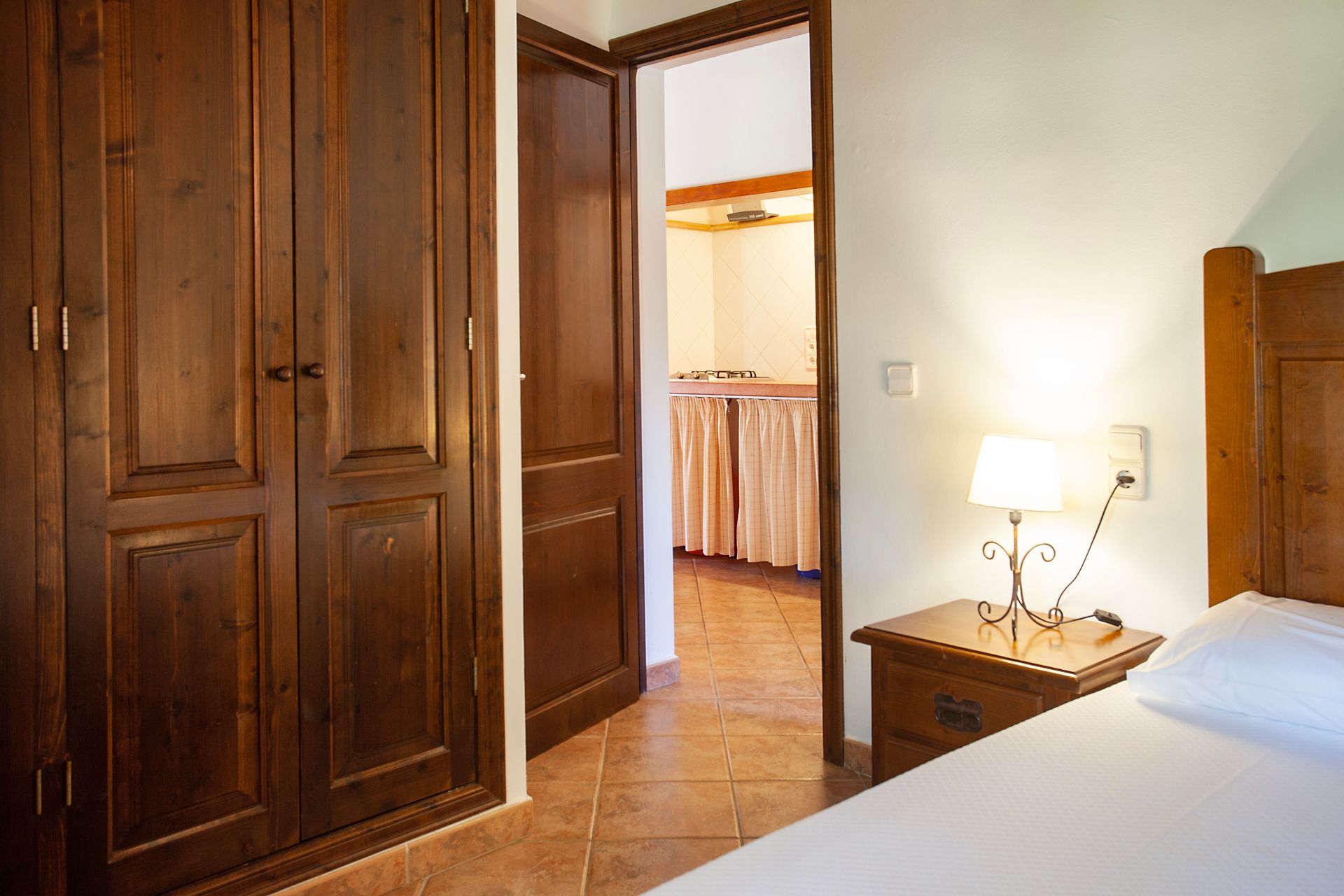 Un dormitorio con cama, mesita de noche, lámpara y armario.