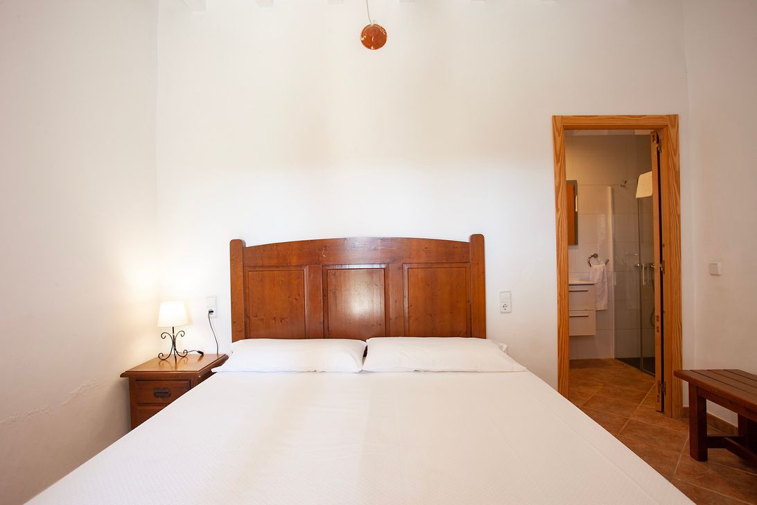 Un dormitorio con una cama, mesita de noche, lámpara y puerta que da a un baño.