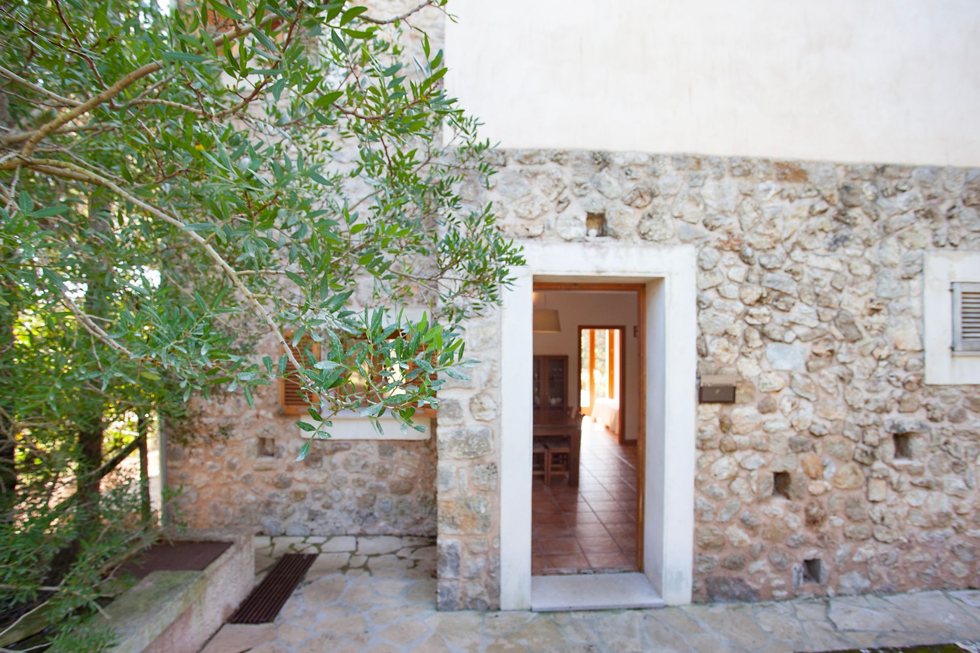 Un edificio de piedra con una puerta abierta y un árbol delante de ella.