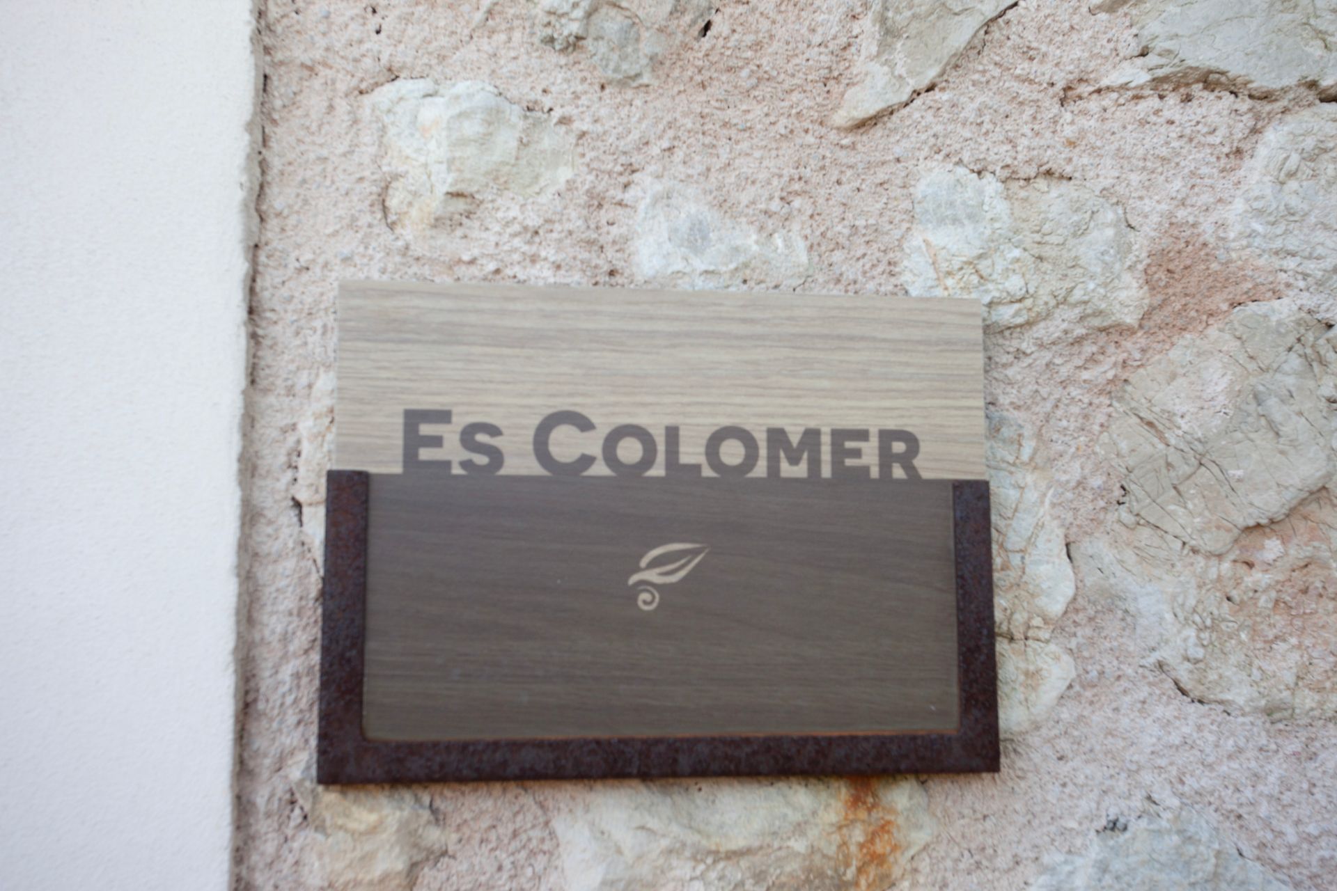 Ein Holzschild an einer Steinmauer sagt Es Colomer