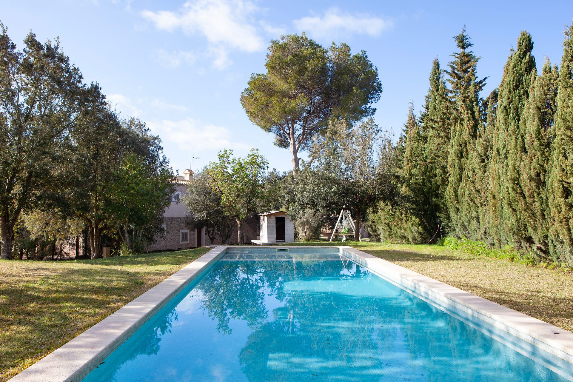 Una gran piscina rodeada de árboles y césped con una casa al fondo.