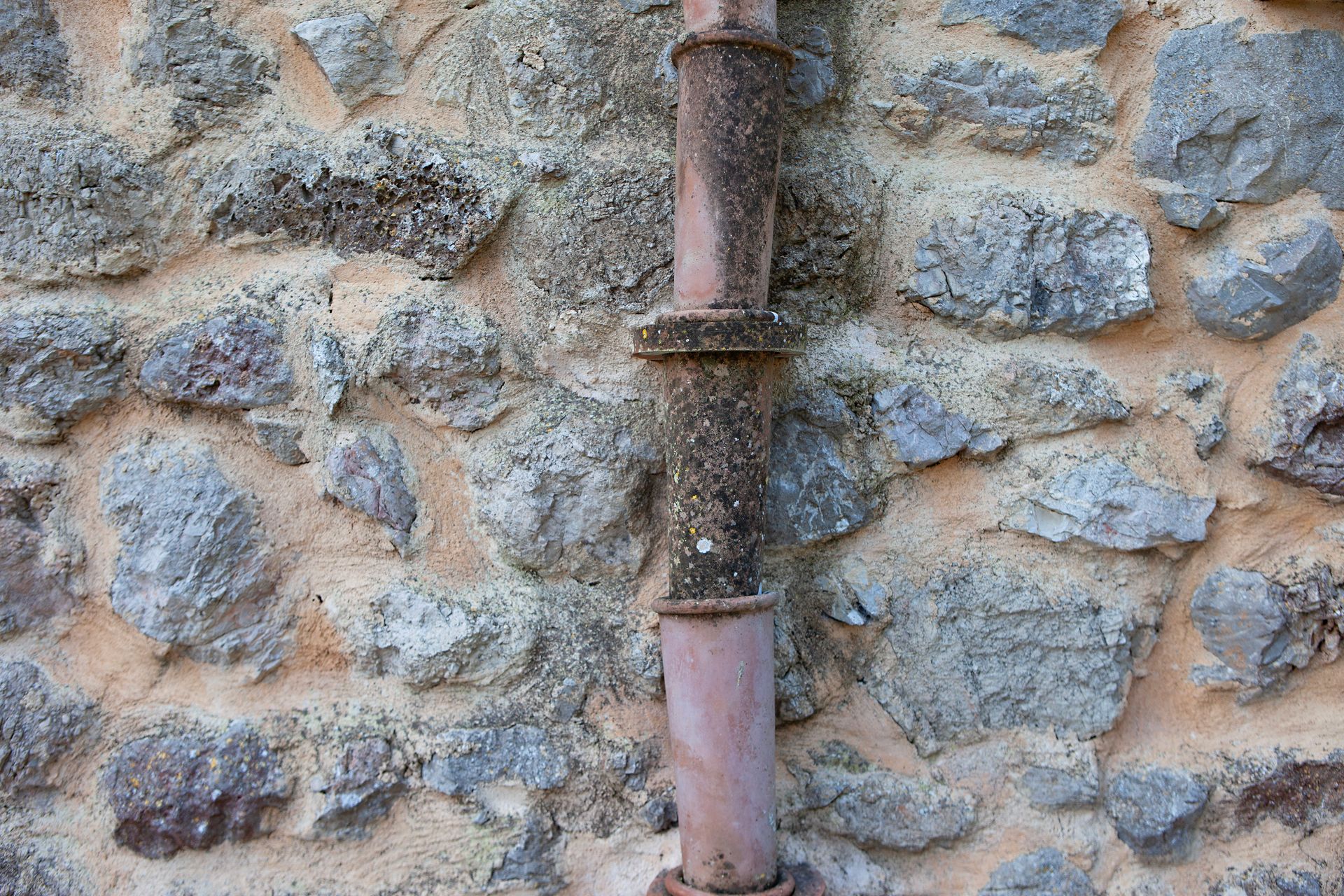 Una tubería oxidada cuelga de una pared de piedra.
