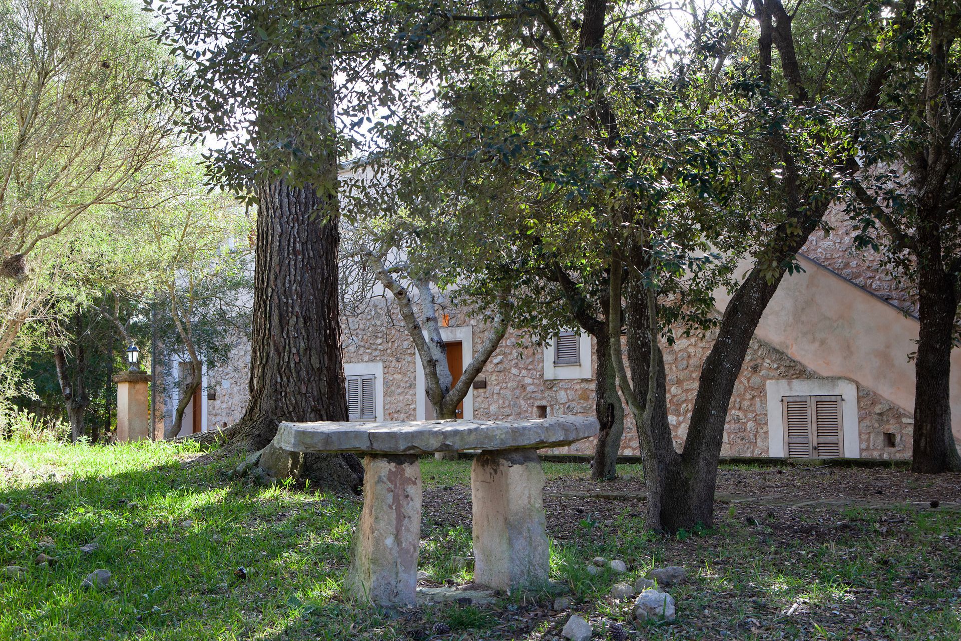 Una mesa de piedra está colocada en el césped frente a un edificio de piedra rodeado de árboles.