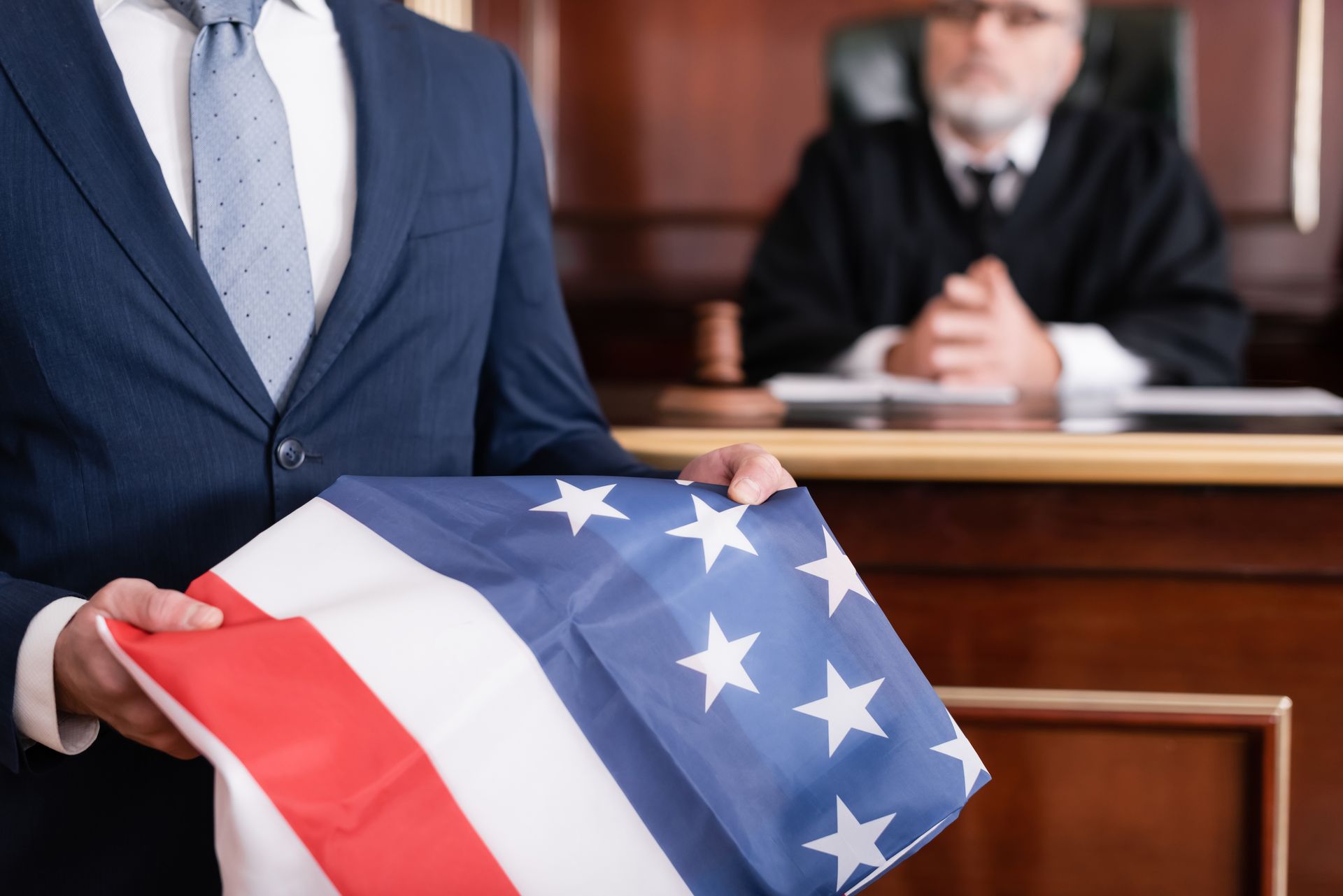 Man in suit holding an American flag in a courtroom, with the judge in the background.