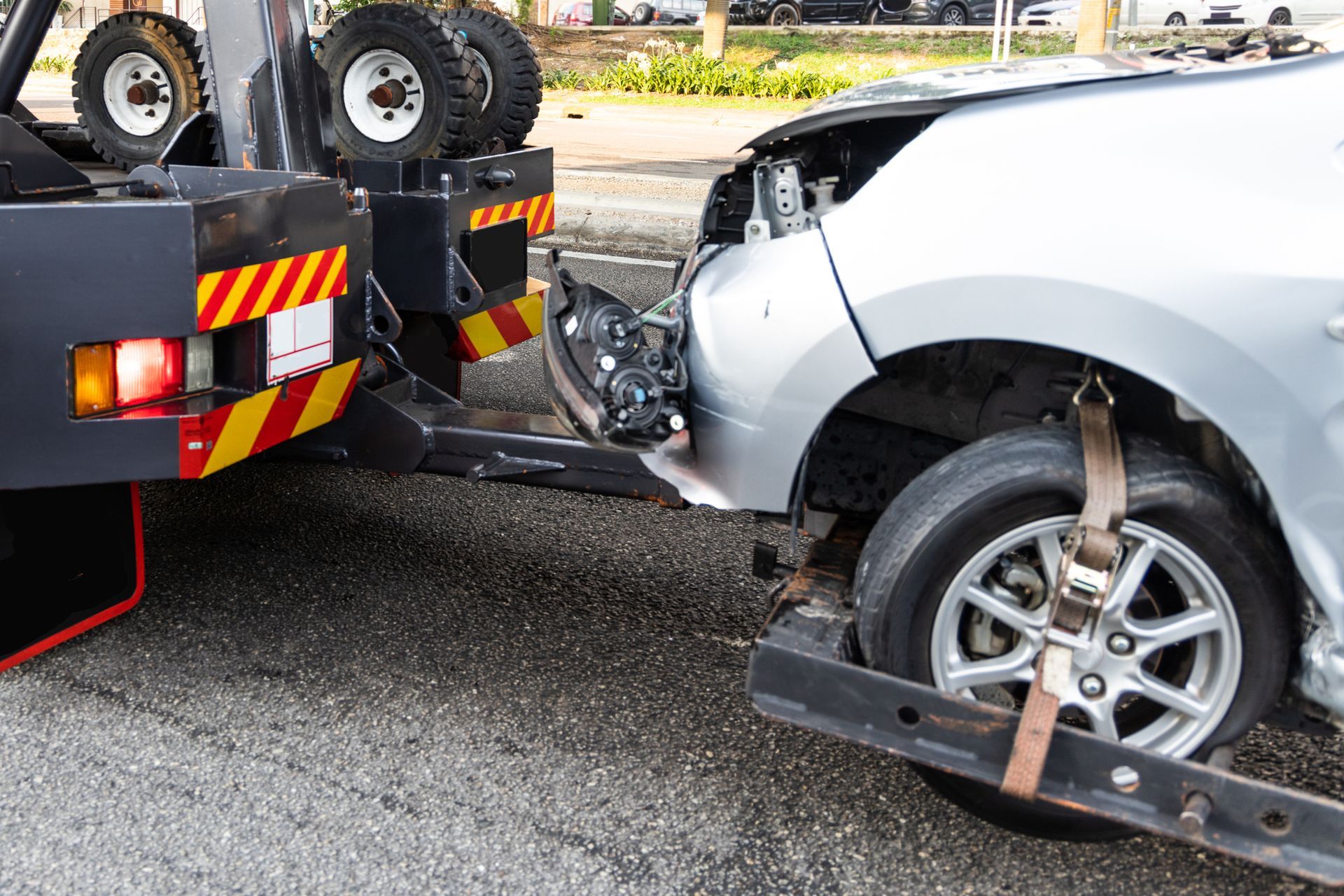 A tow truck is towing a damaged car on the side of the road.