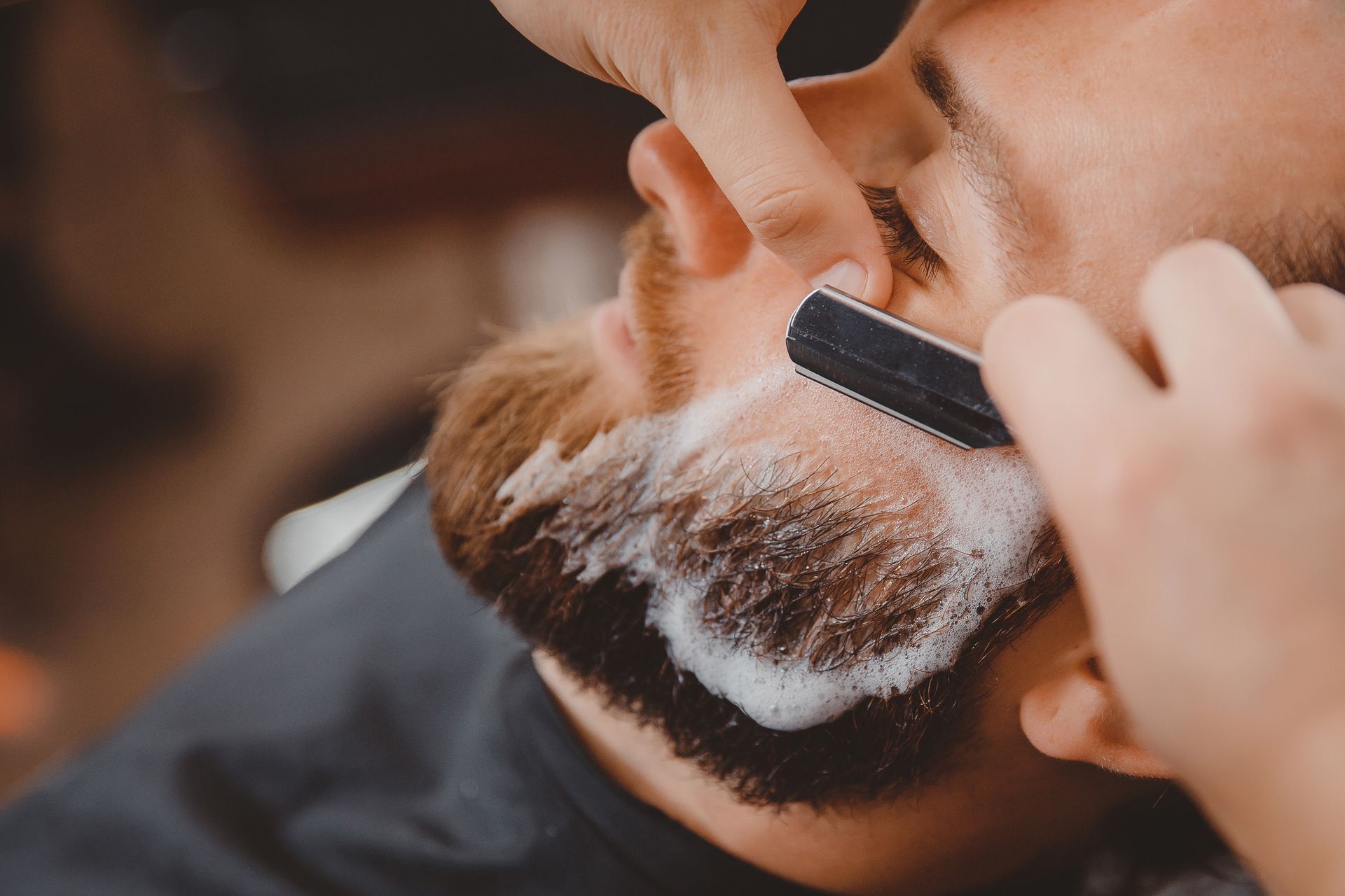 A man is getting his beard shaved by a barber with a razor.