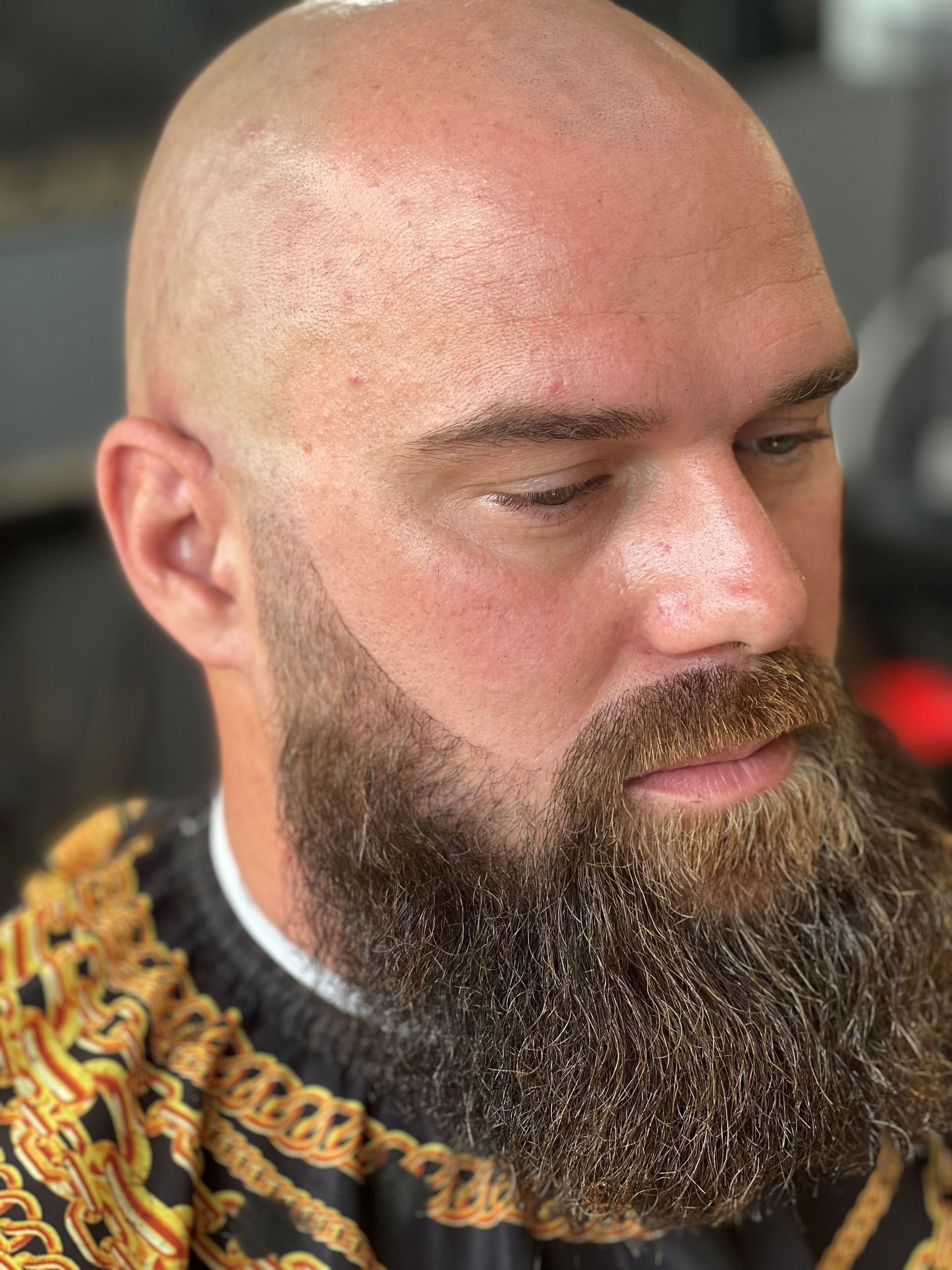 A bald man with a beard is wearing a black and gold sweater.