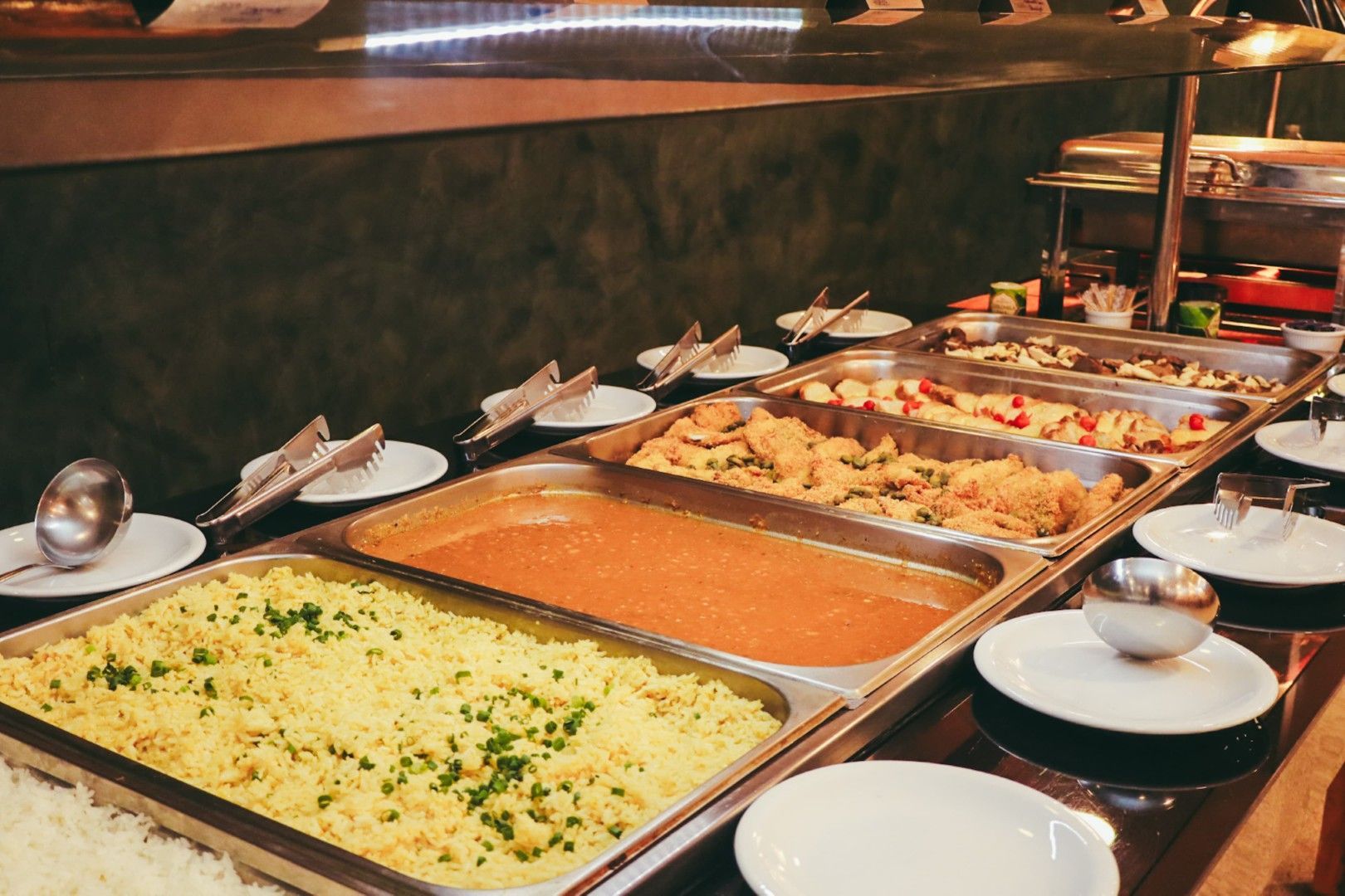 Buffet com diversas opções de comida, incluindo arroz, curry e legumes, em um ambiente de restaurante.